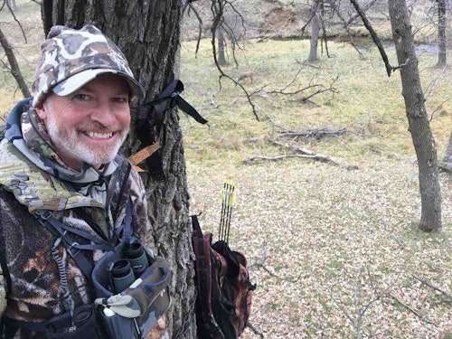 The author was joined by one of his buddies in his favorite treestand tree. The forked oak with numerous large branches holds two hang-on portables, one at 14 feet, and one at 16 feet. Paul (shown) is in the lower stand while the author snapped a pic from the higher one. Can you see the single deer in the background? Although this river-bottom is flat, and whitetails often walk on all sides of the forked oak, the deer never spot the hunters because of the outstanding cover provided at treestand height.