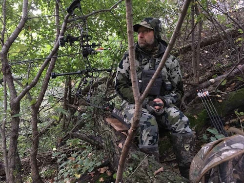 Swamps are great places for a ground ambush, and the same is true for hilly hardwoods. Here, the author’s hunting buddy sits on a fallen log on a very steep hill overlooking a river-bottom deer trail on public land. The hillside provides backdrop cover for the hunter, and he can draw undetected by waiting for an approaching deer to walk behind a large tree.
