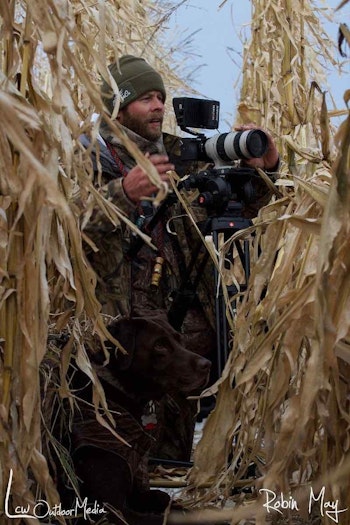 Camera (and dog!) at the ready, Matthew Bielski hides in standing corn while waiting for mallards. (Photo by Robin May)