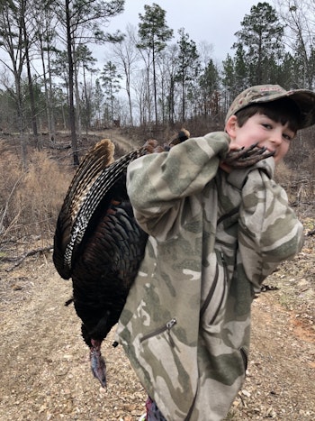 The writer's 10-year-old son carries his first gobbler to the truck. Photo: Mark Olis 
